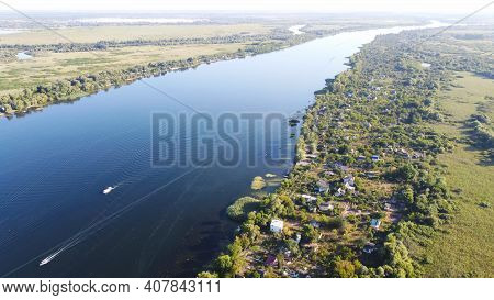Drone Fly Over Waving River Of Blue Color Surrounded By Local Village With Various Buildings And Wet
