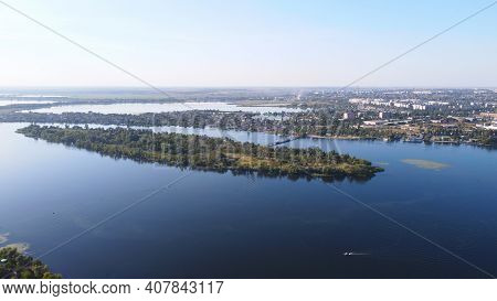 Drone Fly Over Waving River Of Blue Color Surrounded By Local Village With Various Buildings And Wet