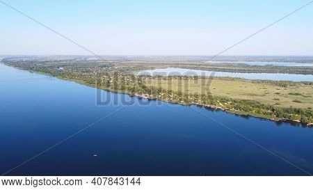 Drone Fly Over Waving River Of Blue Color Surrounded By Local Village With Various Buildings And Wet