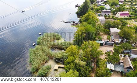 Drone Fly Over Waving River Of Blue Color Surrounded By Local Village With Various Buildings And Wet