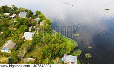 Drone Fly Over Waving River Of Blue Color Surrounded By Local Village With Various Buildings And Wet