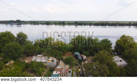 Drone Fly Over Waving River Of Blue Color Surrounded By Local Village With Various Buildings And Wet