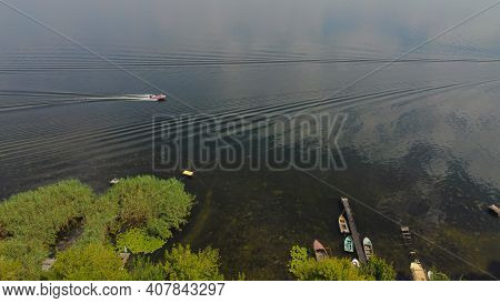 Drone Fly Over Waving River Of Blue Color Surrounded By Local Village With Various Buildings And Wet