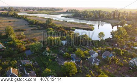 Drone Fly Over Waving River Of Blue Color Surrounded By Local Village With Various Buildings And Wet
