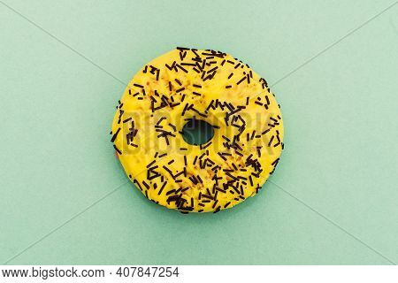 Yellow Donut Decorated With Chocolate Sprinkles Isolated On Green Background. Flat Lay. Top View