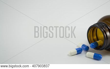 Blue And White Pills Sprinkling Near A Bottle Of Pills On A White Background