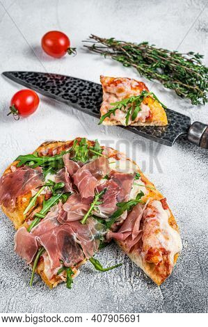 Italian Pizza With Parma Ham, Arugula And Cheeseon A Kitchen Table. White Background. Top View