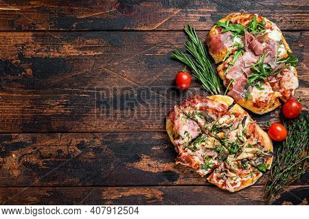 Sliced Pizza With Prosciutto Parma Ham, Arugula And Parmesan Cheese. Dark Wooden Background. Top Vie