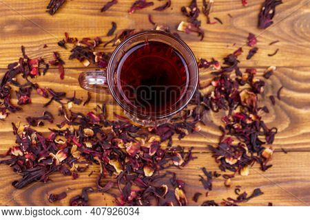 Glass Cup Of Red Hibiscus Tea (carcade, Roselle) On Wooden Table