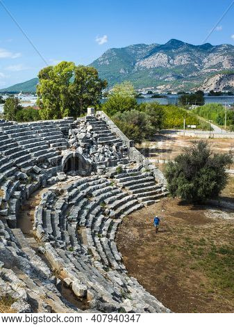 Tourist walking along ruins of Theatre in Letoon Ancient City in village Kumluova, Turkey. Sunny day, Greek culture ancient amphitheater architecture vertical photo