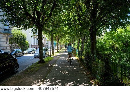 Strasbourg, France - July 29, 2017: Rear View Of Single Woman Cycling On The French Trottoir Under B
