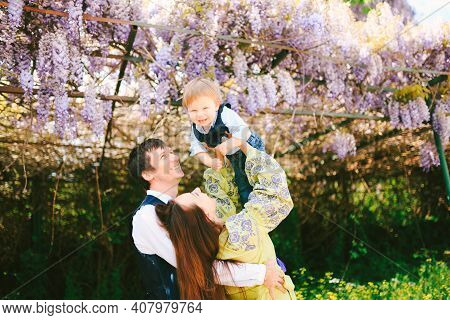 Baby Boy Is Flying In His Mothers Arms Under A Wysteria Tree On A Sunny Day