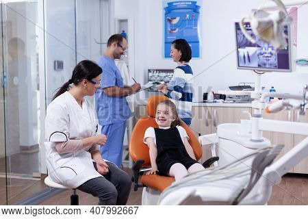 Dentist In Dental Office Making Little Girl Laugh Child With Her Mother During Teeth Check Up With S