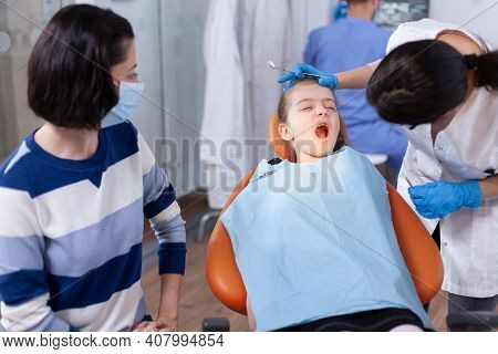 Dental Doctor Checking Tooth Hygine Of Kid With Open Mouth Sitting On Chair. Dentistry Specialist Du