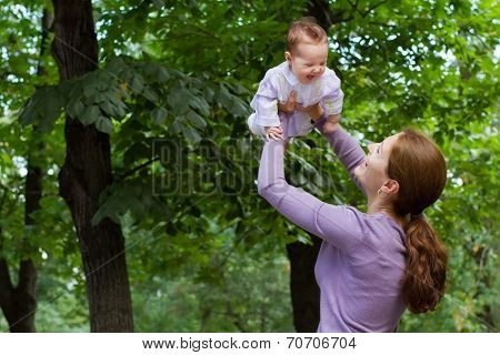 Young Mother Playing With A Laughing Baby Girl In A Park
