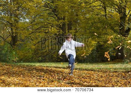 Boy Jumping And Playing With Golden Autumn Leaves