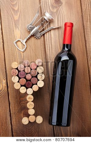 Red wine bottle, glass shaped corks and corkscrew. View from above over rustic wooden table background