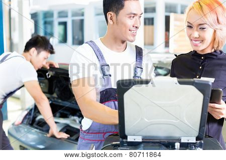 Asian Chinese car mechanic team checking auto engine with diagnostics tool in his workshop