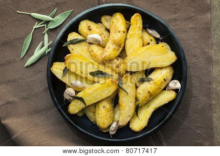 Roasted fingerling or kipfler potatoes, with sage leaves.  Black dish, overhead view.