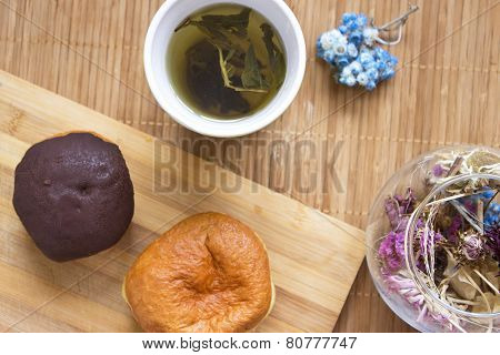 Breakfast. Green tea in orange cup and donuts in chocolate on wooden background.