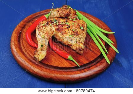 roast meat : chicken legs garnished with green onion pens and peppers on wooden plate over blue wooden background