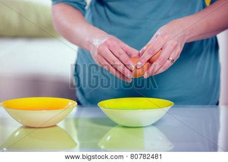 Female hands separating yolk and white of a cracked egg