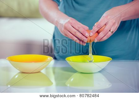 Female hands separating yolk and white of a cracked egg