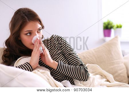 Portrait of a sick woman blowing her nose while sitting on the sofa