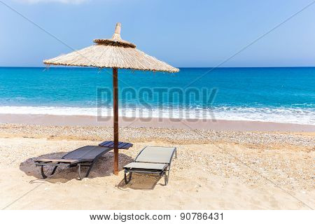 Reed beach umbrella with two loungers on beach at sea