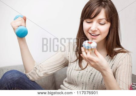 Woman Exercising On Sofa With Cupcake In Hand