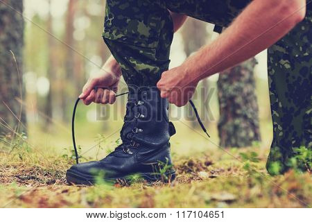 close up of soldier tying bootlaces in forest