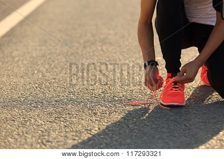 young sports woman runner tying shoelace on city road