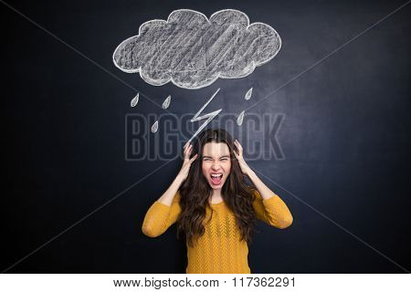 Angry young woman with long hair screaming over blackboard behind her