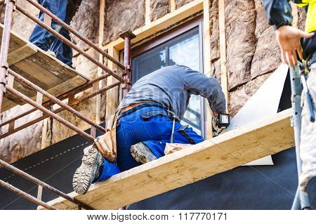 Construction workers thermally insulating house facade with glass wool.