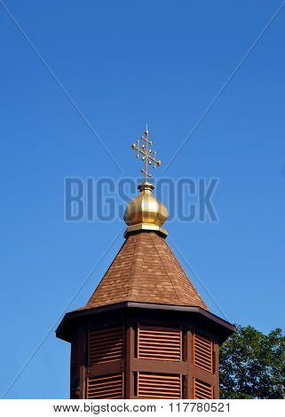Gold cross shaped finial tops the dome on the Byzantine Rite Chatholic Monastery near Eagle Rivers Michigan. Blue sky frames monastery.