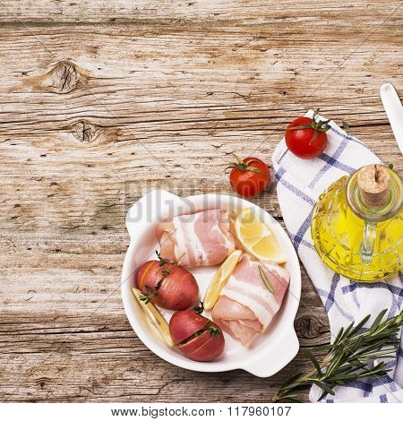 Rolls of chicken wrapped in bacon in baking dish with potatoes stuffed with herbs on a simple wooden background in okruschenii Sweda and vegetable oil in a jug. Selective focus. View from above