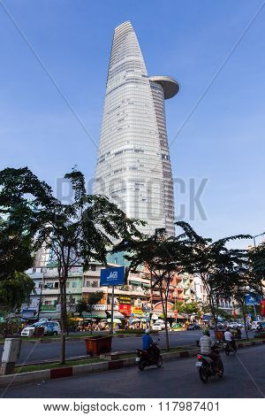 People are riding their motorbikes down the street with Bitexco Financial Tower on background