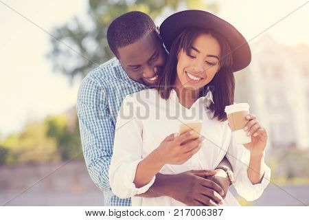 Warm feelings. Joyful nice happy man standing behind his girlfriend and smiling while expressing his feelings