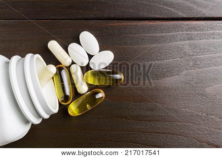 White and yellow capsules of glucosamine omega-3 pills of calcium on plastic box glass with water at wooden table top view.