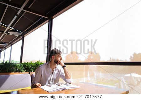Satisfied magazine editor showing ok geste at cafe table. Personable man with beard wears classic style and looking at camera. Concept of glossy paper edition and writers career.
