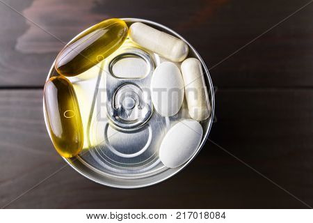 White and yellow capsules of glucosamine omega-3 pills of calcium on plastic box glass with water at wooden table top view.