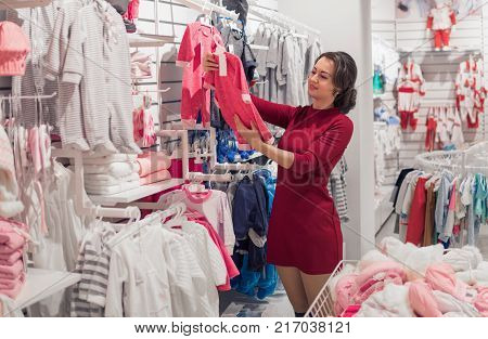 Shopping young woman, manual viewing stand with children's wear in the shop. Buying in the store for kids