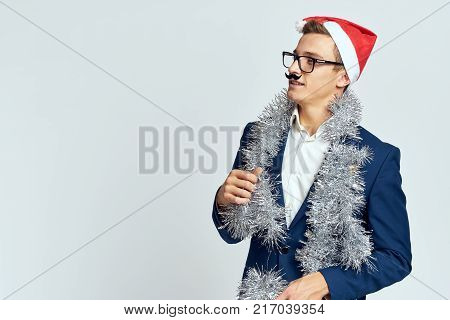 man with artificial mustache, tinsel, new-year hat, light blue background, free space for copying.