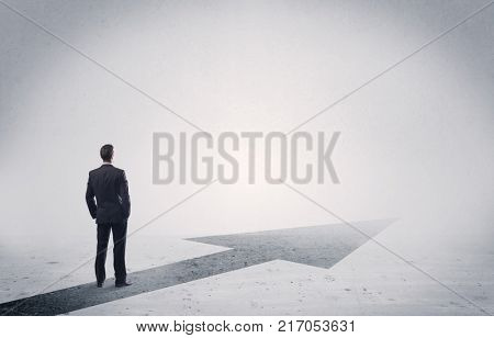 A professional businessman thinking while standing on a black arrow pointing forward in grey space concept