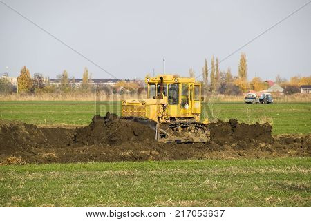 The Yellow Tractor With Attached Grederom Makes Ground Leveling.
