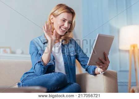 Good connection. Positive cheerful young woman having a good time at home while sitting and waving to her best friend during their video call