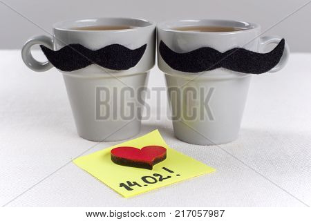 Valentine's day romantic background. A couple of cups of black mustaches - black mustaches, note of text 14.02 written on a paper sticker.
