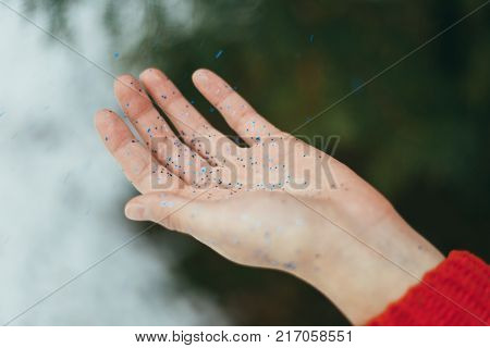 Young beautiful girl blowing on hands with blue glitters on green background.