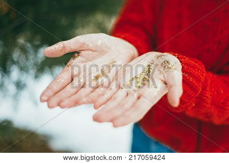 Young curly girl in crystal sunglasses blowing on hands with golden glitters on blue background.