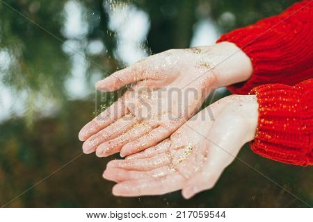 Young curly girl in crystal sunglasses blowing on hands with golden glitters on blue background.
